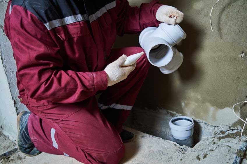 Plumber worker installing sewage pipes in sewerage system sewerage system. Plumber worker installing plastic sewage pipe fitting at construction site