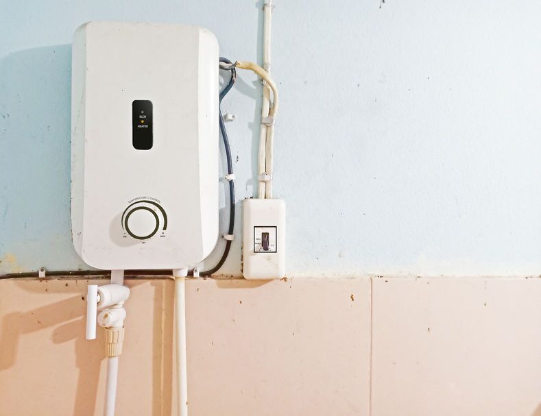 the-advantages-of-tankless-water-heaters-min White instant water heater installed with circuit breaker on the wall of bathroom with free copy space. Safety first concept.