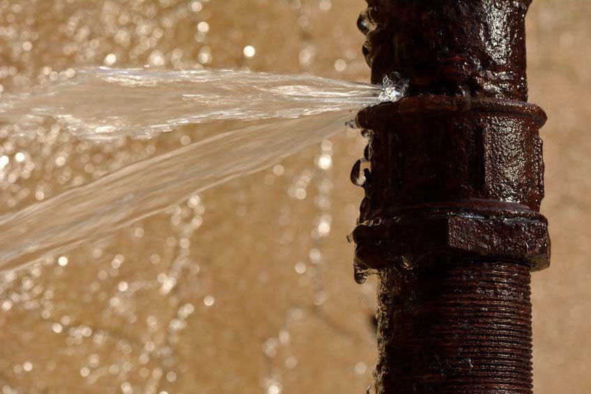 Rusty burst pipe spraying water. Old pipe leaking after freezing in winter Rusty burst pipe spraying water. Old pipe leaking after freezing in winter